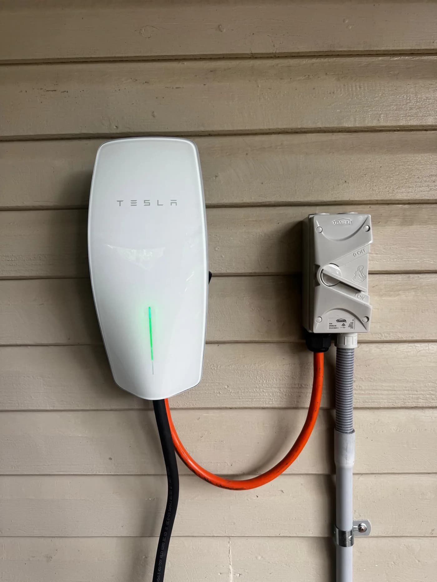 Tesla Wall Connector installed on a weatherboard wall beside its AC isolator